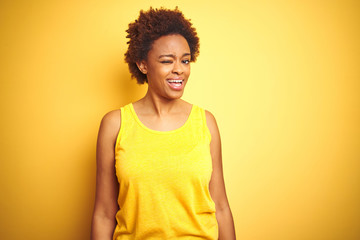 Obraz na płótnie Canvas Beauitul african american woman wearing summer t-shirt over isolated yellow background winking looking at the camera with sexy expression, cheerful and happy face.