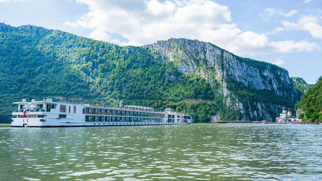 Wei&szlig;es Flusskreuzfahrtschiff auf der Donau im Eisernen Tor Naturpark mit bewaldeten Felsenklippen, Rum&auml;nien