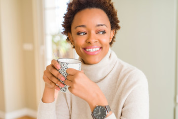 Beautiful young african american woman with afro hair drinking a cup of coffee at home