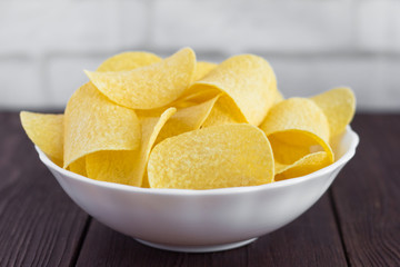 a full bowl of delicious potato chips on a wooden table,close-up