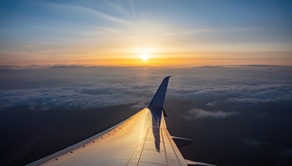 Sunrise view out of an airplane window. Plane flying over the clouds.