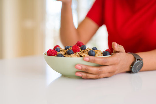 Close up of young woman eating healthy cereals and berries for breakfast