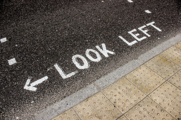 Vintage looking look left sign on London zebra crossing road. Road markings written in white capitals warn pedestrians.