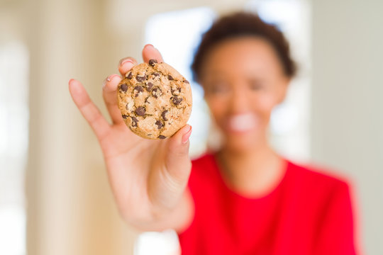 Young african american woman eating chocolate chips cookies with a happy face standing and smiling with a confident smile showing teeth