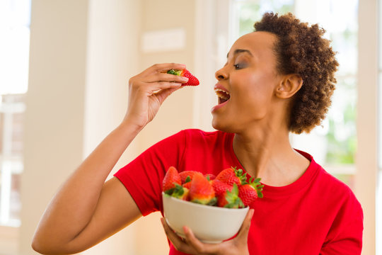 Beautiful young african woman with afro hair eating fresh strawberries