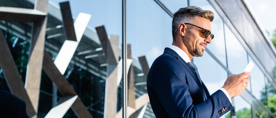 panoramic shot of handsome man in suit and glasses using smartphone