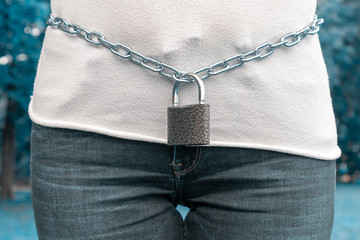 A metal chain with a lock on the lower back of a woman. The female is locked in its middle part in...
