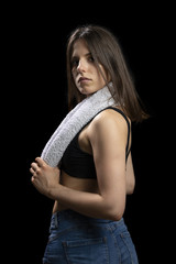 Moody portrait of a sporty young girl with a towel around her neck on a black background.