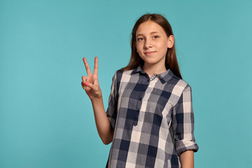 Beautiful teenage girl in a casual checkered shirt is posing against a blue studio background.