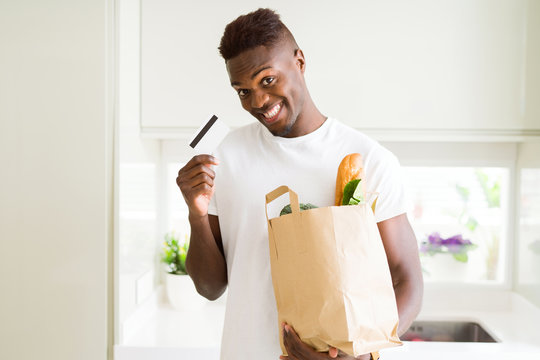 African american man holding paper bag full of groceries and holding credit card as payment