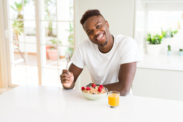 Young african american man eating healthy breakfast in the morning with a happy face standing and smiling with a confident smile showing teeth