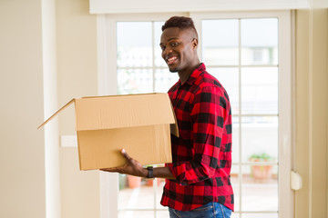 Obraz na płótnie Canvas Young african american man holding a carton box, packing cardboard delivery package at home