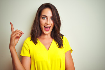 Young beautiful woman wearing yellow t-shirt standing over white isolated background with a big smile on face, pointing with hand and finger to the side looking at the camera.