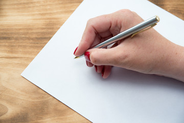 Woman's hand with pen in position to write on blank white paper with room to add text