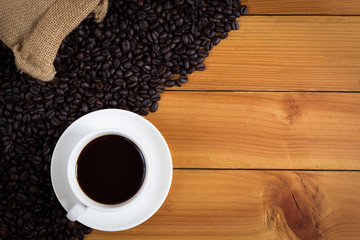 cup of coffee and coffee beans in a sack on wood background, top view.