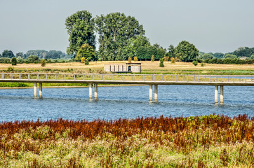 View of a concrete bridge for cyclists and pedestrians as well as a wooden bird watching hut in Vreugederijkerwaard nature reserve near Zwolle, The Netherlands on a sunny summer morning