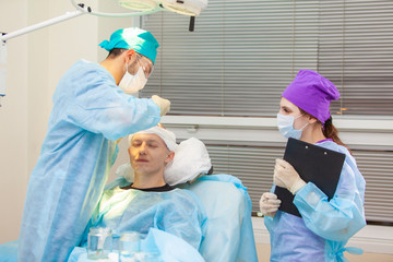 Beautiful portrait of a doctor with documents on the background of the operating room. Baldness treatment. Hair transplant. Surgeons in the operating room carry out hair transplant surgery. Surgical