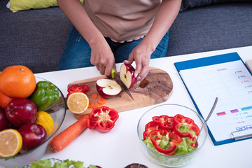 The woman hand cutting red apple,Fresh vegetable was preparing for salad meal ,beside diet plan form,on wooden desk,healthy food,good for life