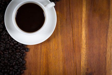 Cup of coffee and coffee beans on wood background, top view.