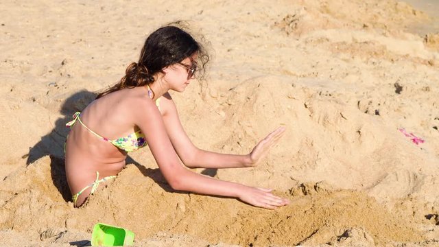 4K A beautiful teen girl is buried in the sand on a beautiful ocean beach