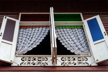 Thai classic wooden and colorful glass window with white knitting curtain and wooden craft.