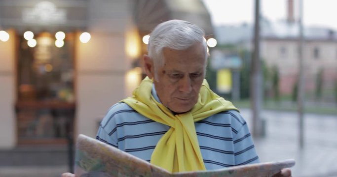 Senior male tourist exploring town with a map in hands and looking for the route