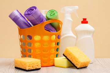 Bottles of dishwashing liquid, basket with garbage bags and sponges on wooden desk.