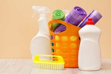 Bottles of dishwashing liquid, basket with garbage bags and sponges on wooden desk.