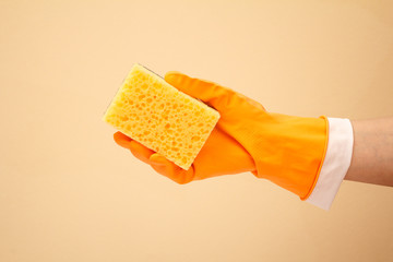 Woman's hand in protective glove with sponge on beige background.