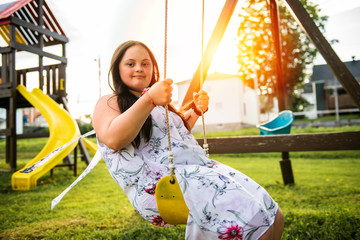 A portrait of trisomie 21 adult girl outside at sunset having fun on a park
