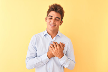 Young handsome businessman wearing elegant shirt over isolated yellow background smiling with hands on chest with closed eyes and grateful gesture on face. Health concept.