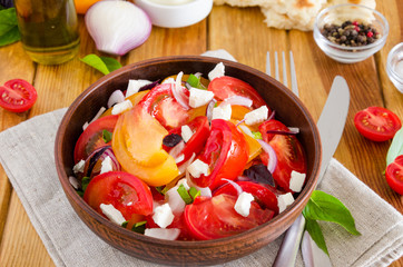 Fresh organic tomato salad with marinated onions, feta cheese and olive oil in a bowl. Rustic style.