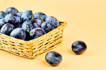 Plums in basket isolated on beige background
