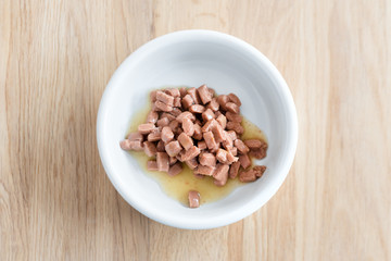 Wet food for cats and dogs in a white bowl on wooden floor close up