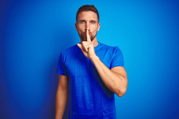 Young handsome man wearing casual t-shirt over blue isolated background asking to be quiet with finger on lips. Silence and secret concept.