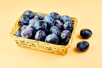 Plums in basket isolated on beige background