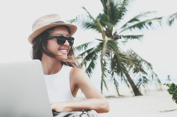 Young woman in a hat working with laptop computer on tropical island beach under palm trees Freelance  concept