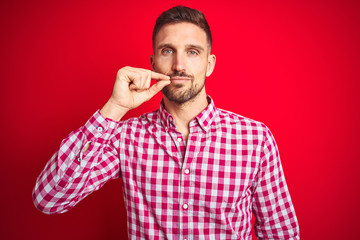 Young handsome man over red isolated background mouth and lips shut as zip with fingers. Secret and...