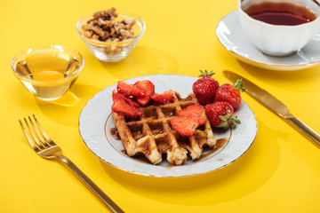 served breakfast with waffle, strawberries, honey, nuts and tea on yellow