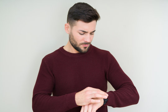 Young handsome man wearing a sweater over isolated background Checking the time on wrist watch, relaxed and confident
