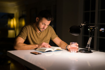 Young handsome man studying at home, reading a book at night - Powered by Adobe