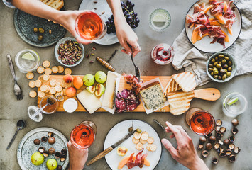 Mid-summer picnic with wine and snacks. Flat-lay of charcuterie and cheese board, rose wine, nuts, olives and peoples hands holding wineglasses and celebrating over concrete table background, top view - 282883749