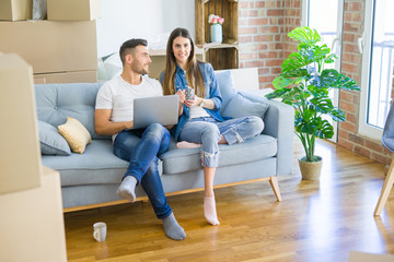 Young couple moving to a new home relaxing sitting on the sofa using computer laptop, smiling happy for moving to new apartment