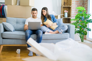 Young beautiful couple relaxing sitting on the sofa of new house using computer laptop with a confident expression on smart face thinking serious