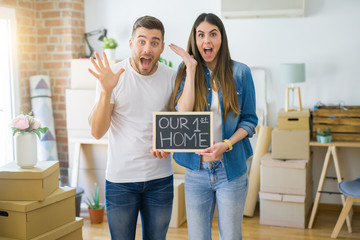 Young beautiful couple holding blackboard with our first home text at new house very happy and excited, winner expression celebrating victory screaming with big smile and raised hands