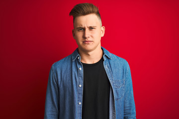 Obraz premium Young handsome man wearing denim shirt standing over isolated red background depressed and worry for distress, crying angry and afraid. Sad expression.