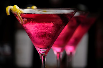 Cropped three cosmopolitan cocktails in line in club on black