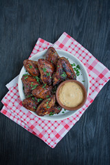 Grilled chicken wings with sauce and herbs.Baked chicken wings in pan. Dark wooden background. Space for text.