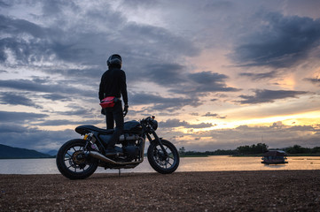 Fototapeta na wymiar Biker standing on vintage big bike with sky at reservoir