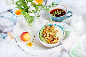 Bowl of fresh oatmeal porridge with kiwi, peach and granola